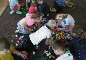grupa dzieci siedzi na dywanie i układa kropki z kolorowych nakrętek